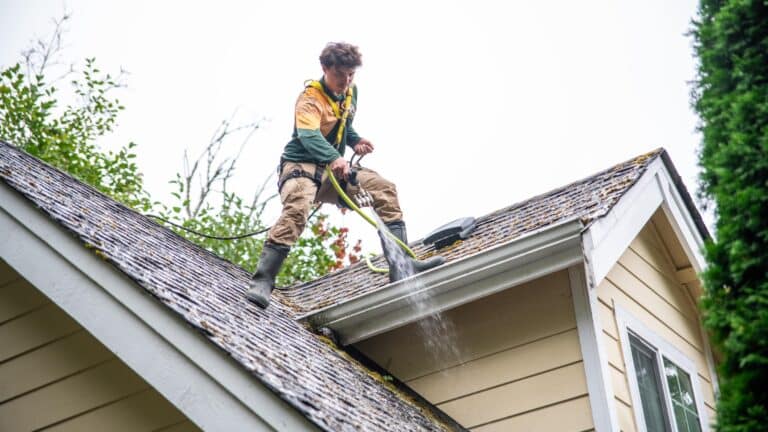 Roof cleaner standing on top of a house using a hose to wash shingles.