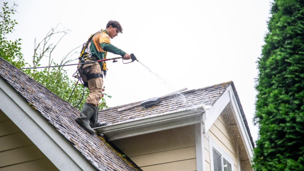 Person conducting rooftop maintenance by washing tiles with water.