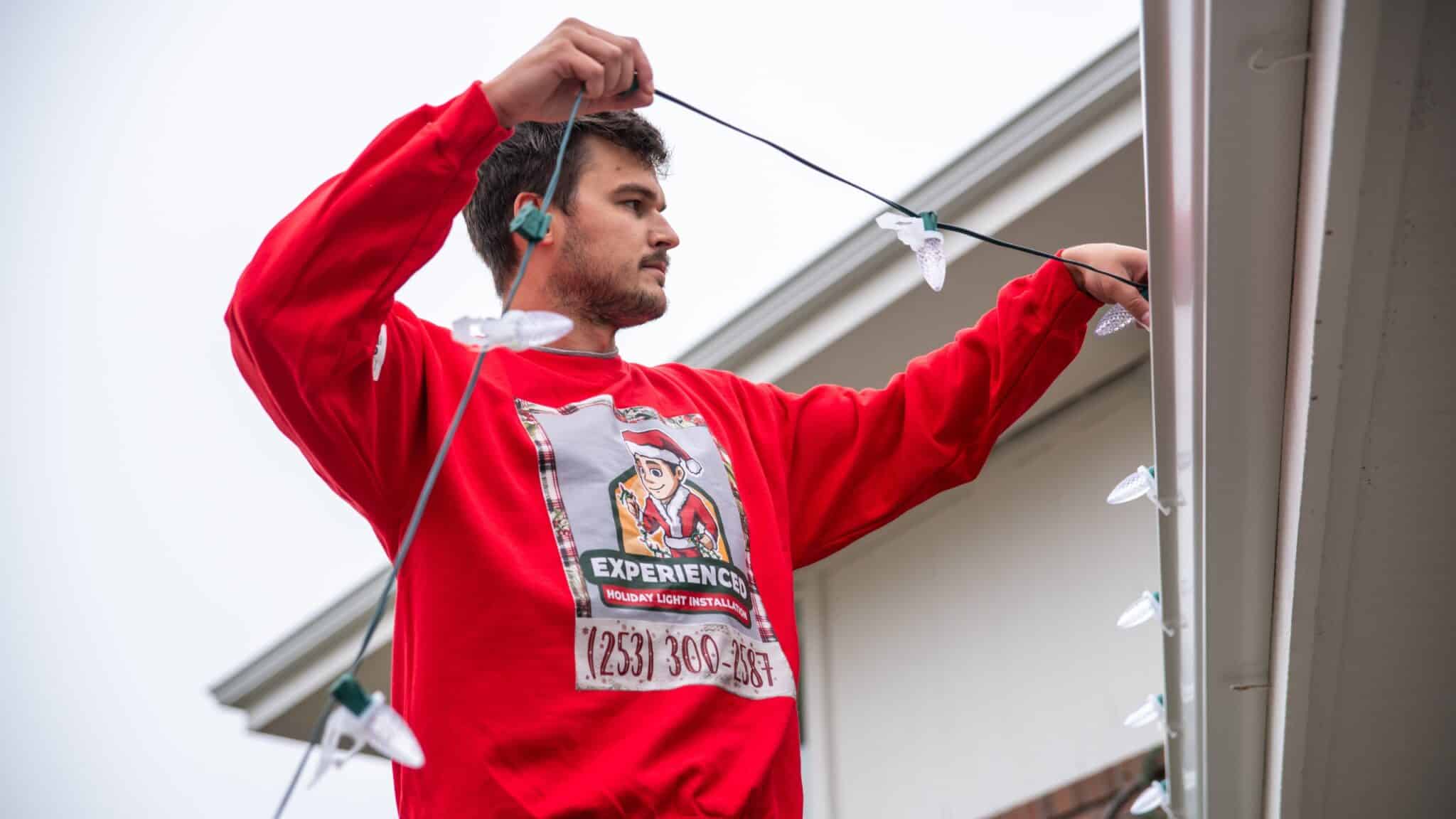 Professional setting up exterior lighting along roofline for seasonal display.